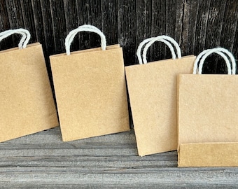 May include: Five brown paper bags with white string handles. The bags are arranged in a row on a wooden surface.