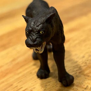 May include: Black panther figurine with a snarling expression and yellow eyes. The figurine is made of plastic and is about 5 inches tall.