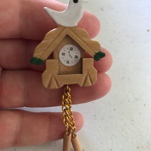 May include: A small wooden cuckoo clock with a white bird on top. The clock face has Roman numerals and a gold chain hangs from the bottom with two wooden weights.