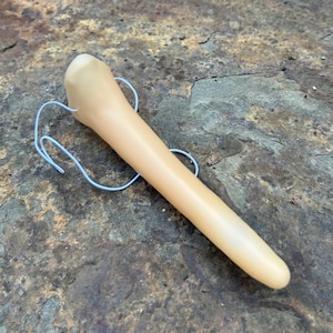 May include: A pale beige, elongated object with a rounded end and a thin, light blue wire attached. The object is made of a smooth material and is on a rough, textured surface.