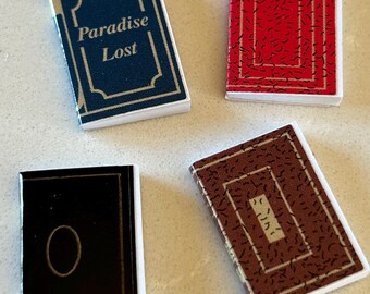 May include: Four miniature books with different colored covers. The covers are decorated with a gold border and a pattern. One book has the title "Paradise Lost" on the cover.