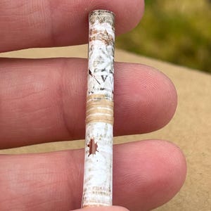 May include: A close-up of a small, rolled-up scroll with a white background and brown and beige patterns. The scroll has a brown stain on the front.