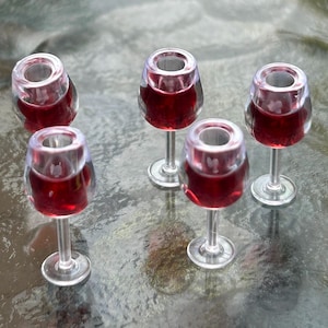 Könnte beinhalten: Fünf klare Weingläser aus Glas, gefüllt mit Rotwein. Die Gläser sind in einem Halbkreis auf einer grauen, strukturierten Oberfläche angeordnet.