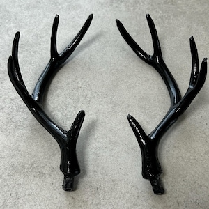 May include: Two black, plastic deer antlers. The antlers are curved and have a glossy finish.