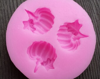 May include: Pink silicone mold with three cavities shaped like a stylized pumpkin. The mold is designed for making edible decorations.