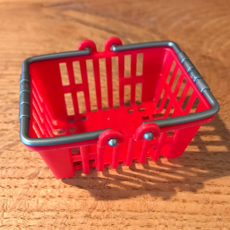 Op de afbeelding: Een klein rood plastic winkelmandje met zilveren handvatten. Het mandje is leeg.