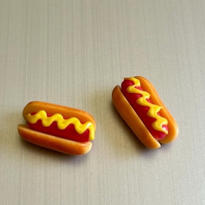 Puede incluir: Dos mini hot dogs con mostaza amarilla encima, sobre una superficie marrón claro.