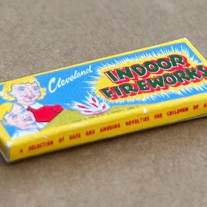 May include: A yellow box with the words "Cleveland Indoor Fireworks" printed on it. The box has a blue background with a picture of a girl and a boy. The text "A selection of safe and amusing novelties for children of all ages" is printed on the bottom of the box.