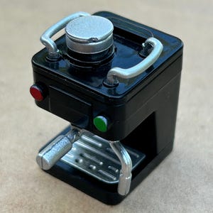 May include: A black espresso machine with a silver handle and a silver top. The machine has a red and green light.