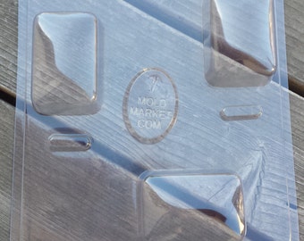 Puede incluir: Molde de plástico transparente con cuatro cavidades rectangulares para hacer jabón u otras manualidades. El molde tiene un logotipo que dice "Mold Market.com".