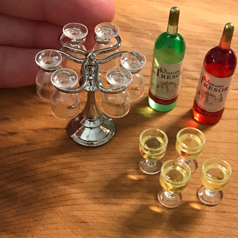 May include: A silver metal wine glass holder with six clear glass wine glasses. Two bottles of wine, one green and one red, are on a wooden surface. Four clear glass wine glasses are filled with a yellow liquid.