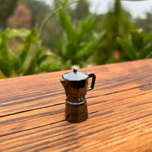 Könnte beinhalten: Eine schwarze Miniatur-Espressomaschine aus Metall auf einer Holzoberfläche.