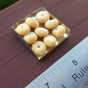May include: A small silver tray filled with nine miniature powdered donuts. The tray is sitting on a wooden surface next to a metal ruler.