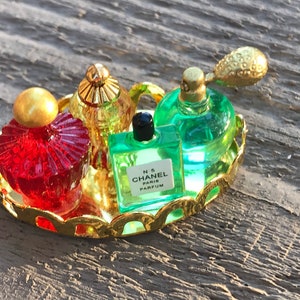 May include: A gold-colored tray with four miniature perfume bottles. The bottles are red, green, clear, and gold. The tray has a decorative scalloped edge.