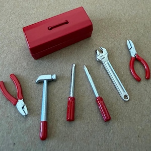 May include: A miniature red rectangular toolbox accompanied by a set of six small tools, including a hammer, an adjustable wrench, two pairs of pliers with red handles, and two screwdrivers with red handles, all featuring metallic silver finishes.