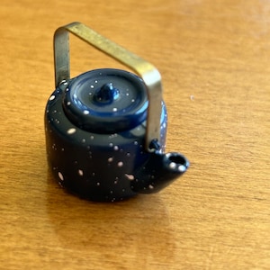 May include: A small blue teapot with white polka dots and a gold handle. The teapot has a lid with a small knob on top.