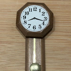 Puede incluir: Un reloj de madera con una esfera blanca y números negros. El reloj tiene un péndulo y está colgado en una pared.