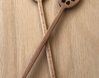 Puede incluir: Dos cucharones de miel de madera con recortes en forma de corazón. Los cucharones son de madera marrón claro y tienen un mango en forma de corazón.