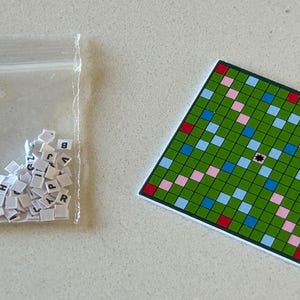May include: A green, blue, pink, and red game board with a black star in the center. A plastic bag filled with white tiles with black letters is next to the board.