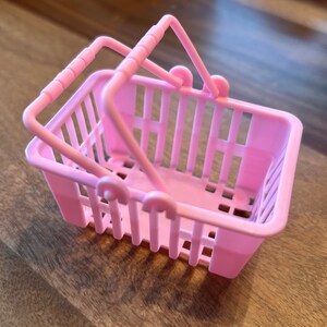 Op de afbeelding: Een klein roze plastic winkelmandje met twee handvatten.