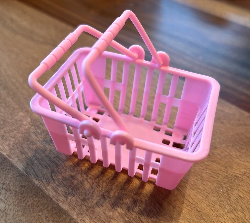 Op de afbeelding: Een klein roze plastic winkelmandje met twee handvatten.