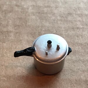 May include: A silver pressure cooker with a black handle. The lid has a black knob and two small silver knobs.
