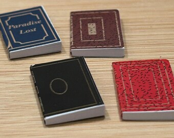 May include: Four miniature hardcover books with different colored covers. The first book has a blue cover with gold lettering that reads "Paradise Lost". The second book has a brown cover with a gold design. The third book has a black cover with a gold design. The fourth book has a red cover with a black design.