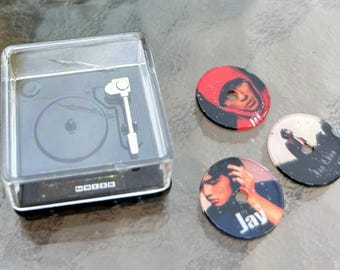 May include: A miniature record player with a clear plastic case and a silver tone arm. Three round discs with images of people are displayed next to the player. The discs have the text "Jay" and "Jigga Man" printed on them.