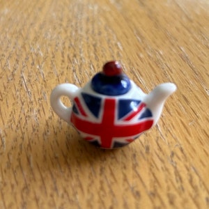 May include: A small white teapot with a red, white, and blue Union Jack design. The teapot has a small red knob on the lid.