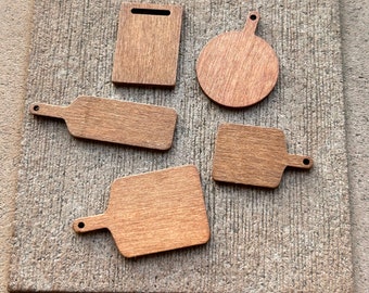 Puede incluir: Cinco tablas de cortar de madera de diferentes formas y tamaños. Las tablas son todas de madera marrón claro y tienen un acabado natural. Las tablas están dispuestas en un patrón aleatorio sobre una superficie texturizada.