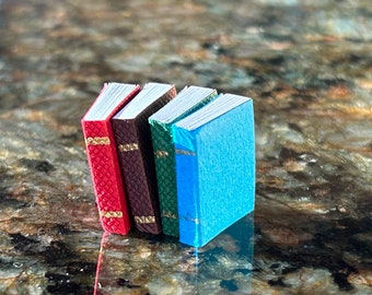 May include: Four miniature books stacked on top of each other. The books are bound in red, brown, green, and blue covers.