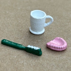 May include: A white ceramic toothbrush holder, a green toothbrush, and a pink ceramic toothbrush holder.