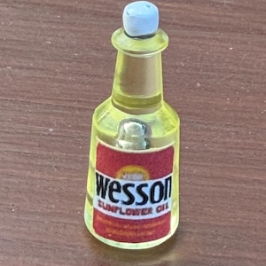 Pode incluir: Uma garrafa em miniatura de pl&aacute;stico amarelo transl&uacute;cido de &oacute;leo de girassol Wesson com uma tampa branca. A garrafa apresenta um r&oacute;tulo retangular vermelho com o texto Wesson e Sunflower Oil impresso em letras pretas e brancas na frente.