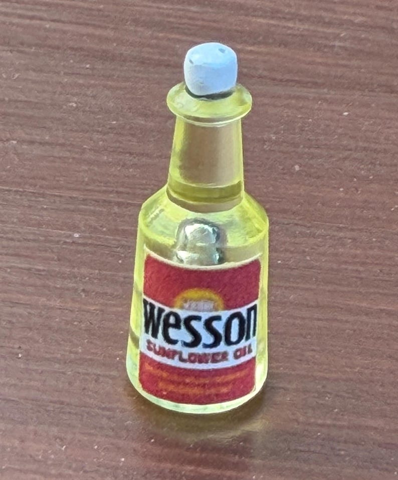 Pode incluir: Uma garrafa em miniatura de pl&aacute;stico amarelo transl&uacute;cido de &oacute;leo de girassol Wesson com uma tampa branca. A garrafa apresenta um r&oacute;tulo retangular vermelho com o texto Wesson e Sunflower Oil impresso em letras pretas e brancas na frente.
