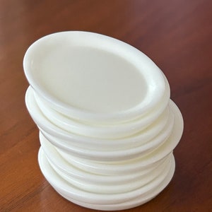 May include: A stack of white, round, plastic plates. The plates are stacked on top of each other, with the top plate being the largest.