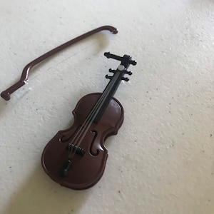 May include: A brown toy violin with a black bow and strings. The violin is lying on a white surface.