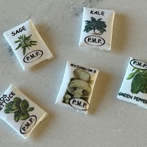 May include: Five white paper packets with black text and illustrations of different vegetables and herbs. The packets are labeled "Sage", "Kale", "Green Pepper", "Mushroom", and "Cos Lettuce". Each packet has a black circle with the text "P.M.P."