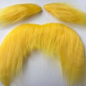May include: A set of bright yellow, fluffy, fake mustache and sideburns. The mustache is a curved shape, and the sideburns are rectangular. The items are likely for a costume or novelty item.