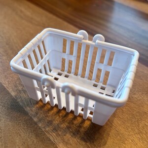 Op de afbeelding: Een witte plastic boodschappenmand met een handvat. De mand is leeg en heeft een rasterpatroon.