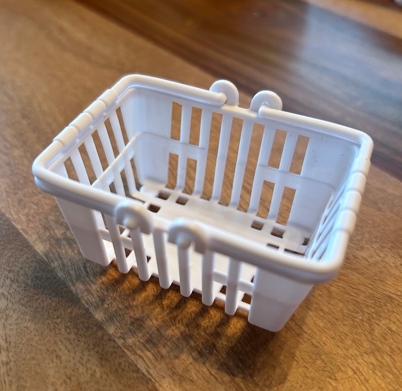 Op de afbeelding: Een witte plastic boodschappenmand met een handvat. De mand is leeg en heeft een rasterpatroon.