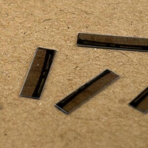 May include: Five small, rectangular, brown circuit boards with gold-coloured connectors. The boards are arranged in a scattered pattern on a brown surface.