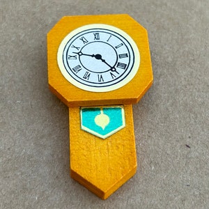 Puede incluir: Un reloj de madera con una esfera dorada y números romanos negros. El reloj tiene un péndulo con un diseño turquesa y dorado.