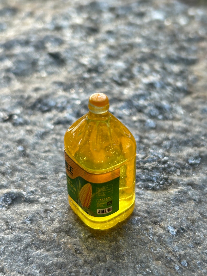 May include: A clear plastic bottle of yellow corn oil with a green label featuring a corn cob. The label has Chinese text and a barcode.