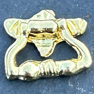Könnte beinhalten: Ein goldfarbener, verzierter Türklopfer mit ringförmigem Griff und dekorativer Frontplatte. Der Klopfer hat eine detaillierte, strukturierte Oberfläche und ist wahrscheinlich aus Metall. Das Design ist klassisch und elegant.