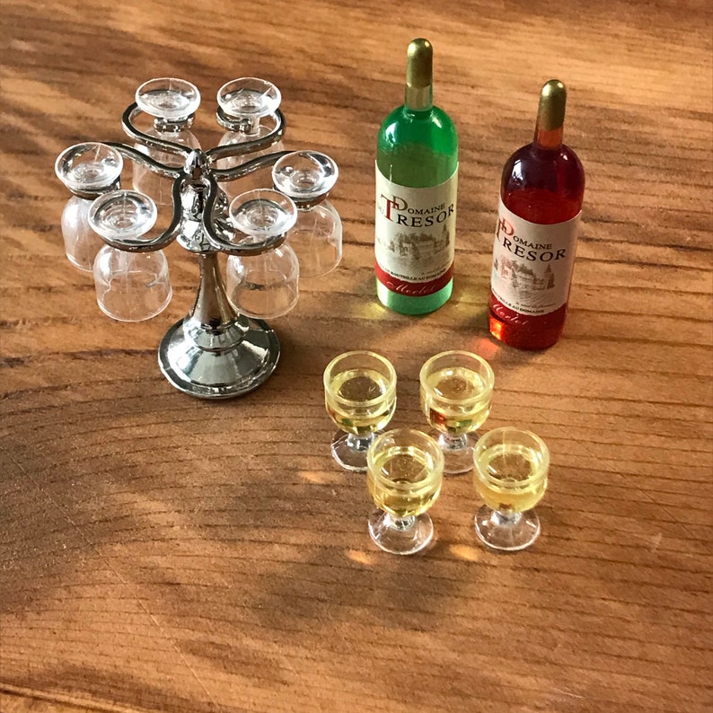 May include: A silver metal wine glass holder with six glasses, two bottles of wine, one green and one red, and four filled wine glasses on a wooden surface.