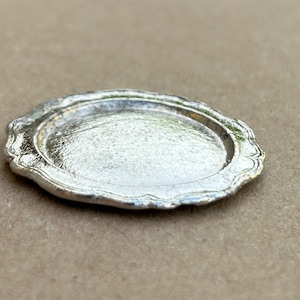 May include: A silver-colored, decorative, round serving tray with a scalloped edge.
