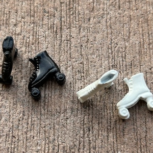 Peut inclure: Quatre patins à roulettes miniatures, deux noirs et deux blancs, sur une surface brune texturée.