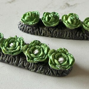 May include: Two miniature garden rows of green cabbage plants with white centers. The plants are arranged in a row on a brown, textured base.