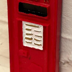 May include: Red vintage-style mailbox with a gold crown and the letters "VR" on the top. The mailbox has a white rectangular panel with gold lines and a black slot for mail.