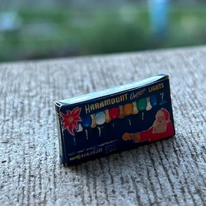 以下が含まれることがあります： 赤い白のポインセチア柄の青い箱で、前面に「Haramount Outdoor Lights 7」の文字が書かれています。箱には、7つのカラフルなクリスマスライトとサンタクロースの図柄が描かれています。